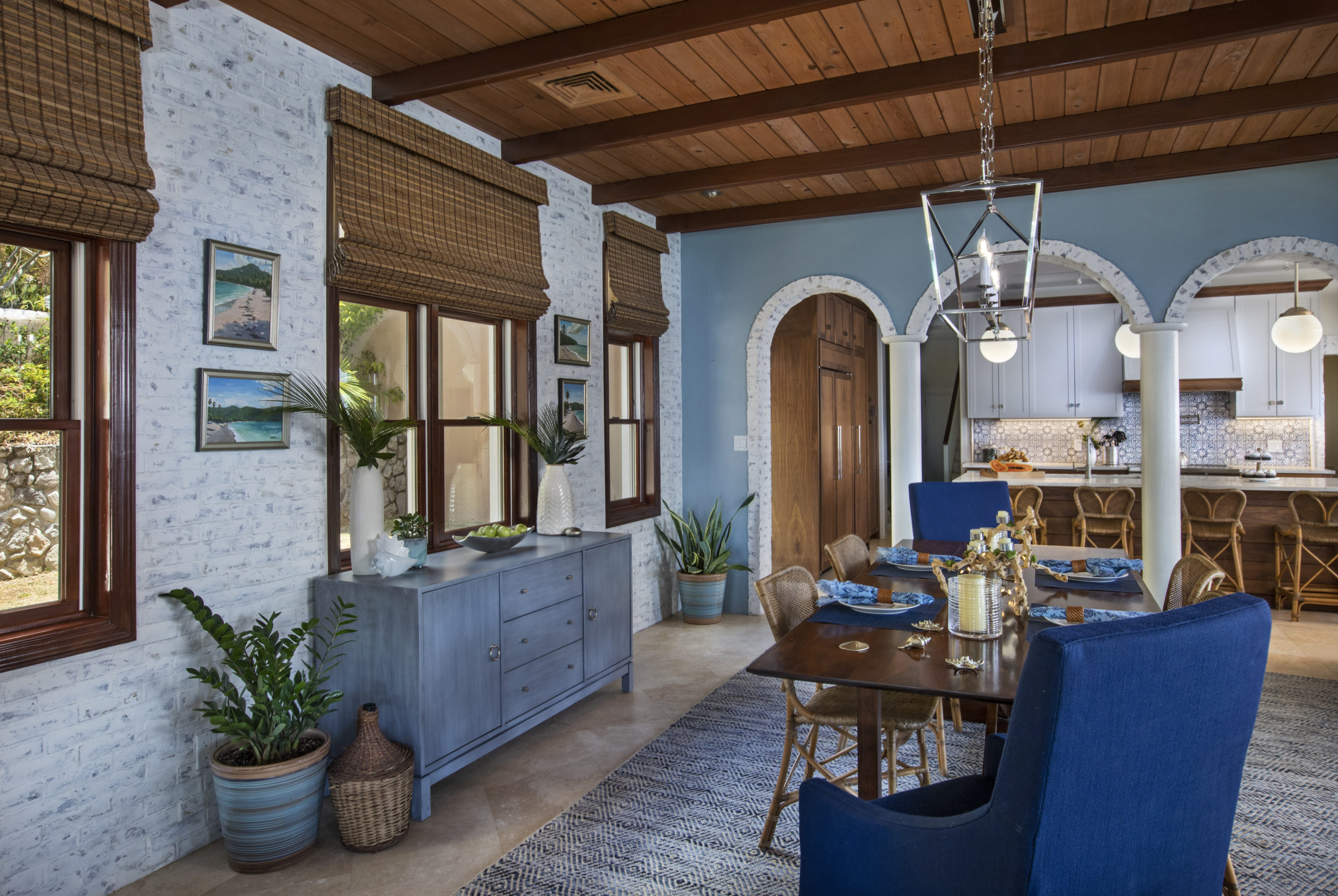 Dining room with lime washed brick work, blue sideboard, slipcovered dining chairs and a blue and white diamond rug.