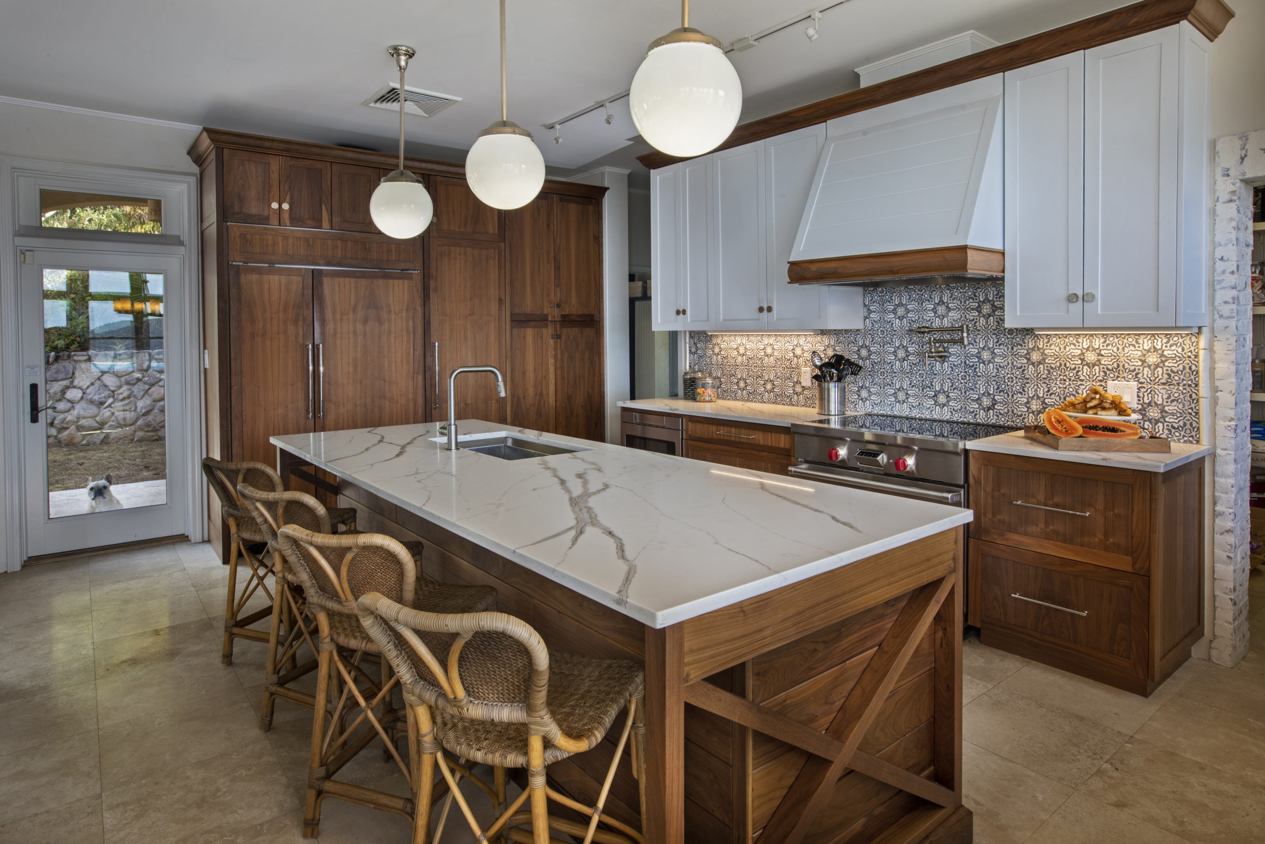 Kitchen with two tone walnut cabinets, a large kitchen island, quartz counter tops, a custom vent hood, blue and white tile back splash and a GE piza oven