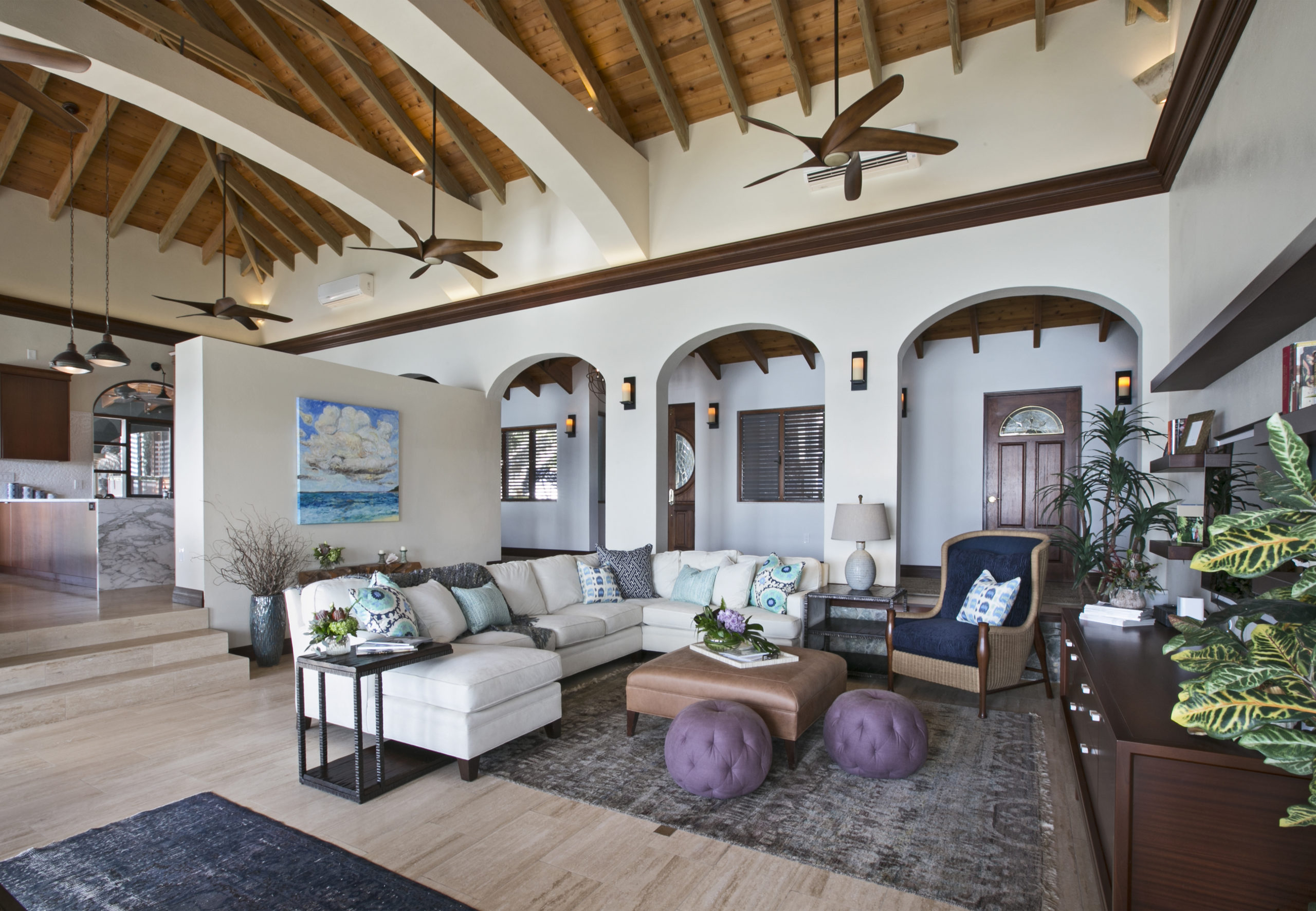 white sectional sofa with blue throw pillows, purple poofs and high ceilings.