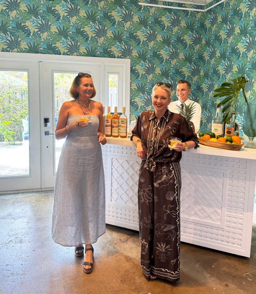 Tiffany Cassidy standing with Danielle Rolins at a drink bar. Wall behind them is covered in Tobago Leaf Caribbean wallpaper by Starboard Lane.